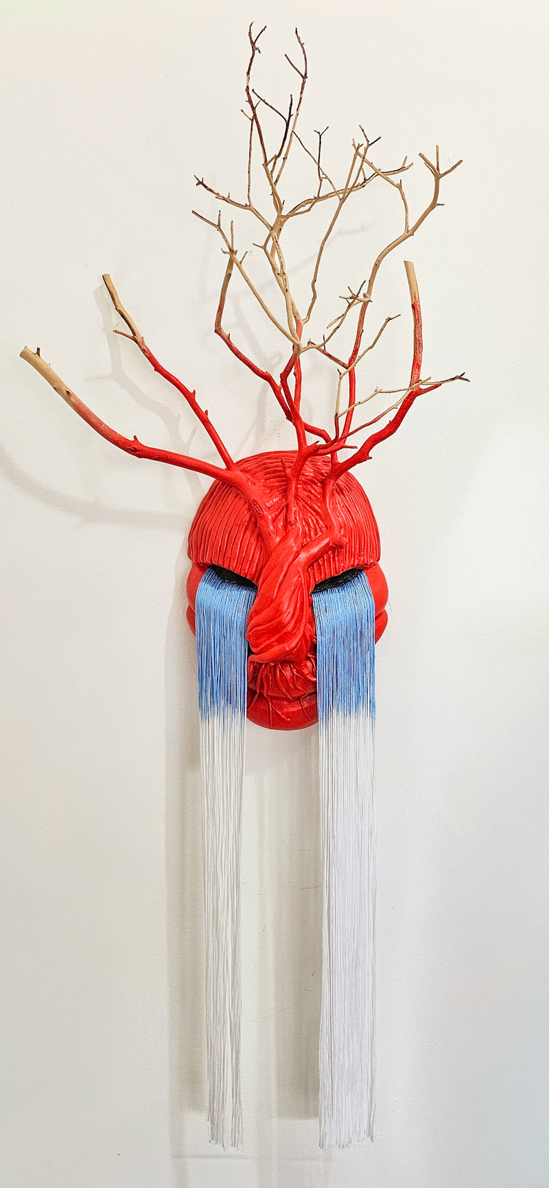 Red clay mask with blue fringe with branches against a white background
