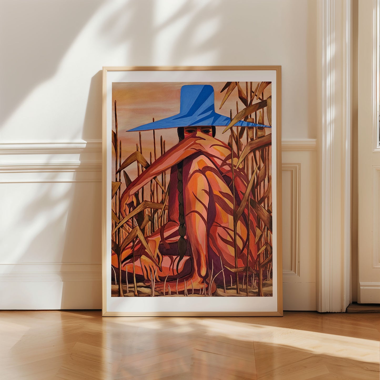 Framed artwork of a person in a blue hat sitting among corn stalks on a white wall.